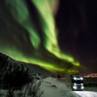 Truck driving at night with aurora in the sky