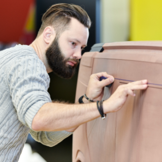 Man with beard and grey sweater working with a model of NXT vehicle