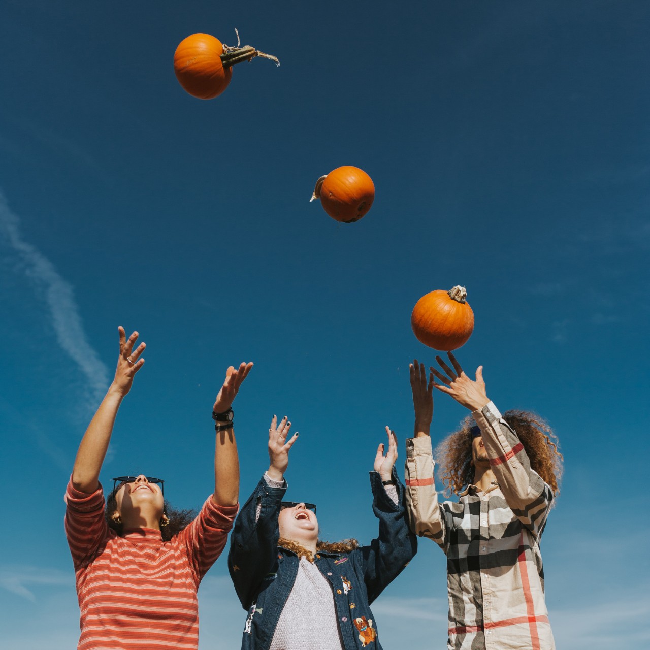 Three persons throwing pumpkins up in the sky