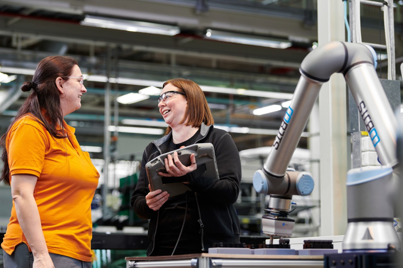 Två medarbetare som står bredvid en robotarm och pratar