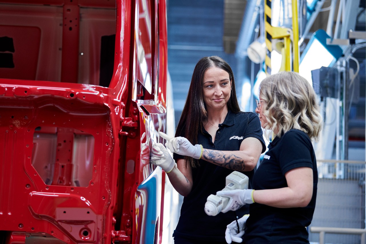 Två medarbetare i vårt Täcklacksmåleri inspekterar en röd hytt